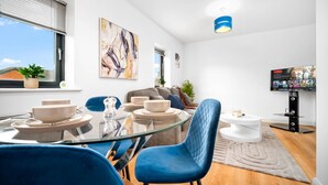 Ein modernes Wohnzimmer mit einem Glastisch, blauen Stühlen, einer Couch, einem Fernseher und Kunstwerken an der Wand.