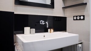 Une salle de bain moderne avec un grand lavabo blanc, un plan de travail noir, un miroir et un radiateur fixé au mur.