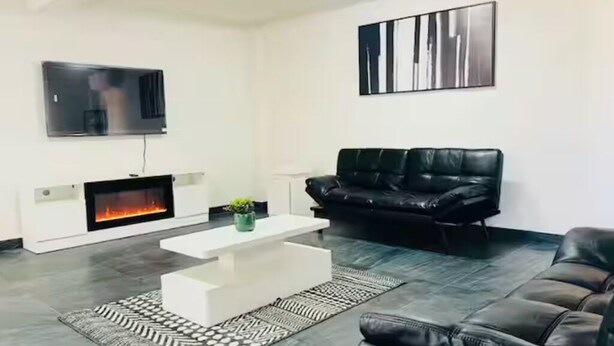 A modern living room with a fireplace, a black leather sofa, a white coffee table, and a patterned rug.