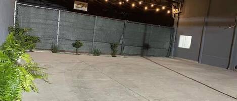 Un patio al aire libre con luces colgantes, cerca de metal y plantas en macetas.