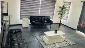 A modern living room with a black leather sofa, a white coffee table, and a large window with blinds.