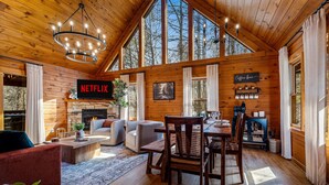 Ein gemütliches Blockhaus-Interieur mit Kamin, Netflix-Logo, Holzwänden und großen Fenstern.