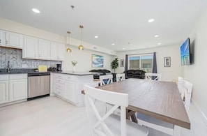 Una cocina moderna con armarios blancos, una mesa de comedor de madera e iluminación colgante.