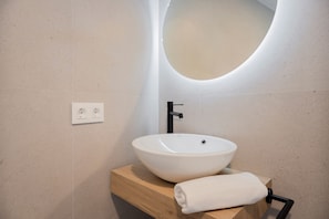 A modern bathroom with a white vessel sink, wooden vanity, and a round mirror. - Hotel ARENA byAstiblanco (Valencia)