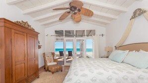 Un dormitorio con una cama grande, un armario de madera, un ventilador de techo y vista al océano a través de un ventanal.