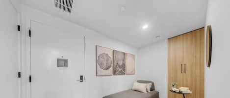 Une chambre moderne avec un canapé gris, une armoire en bois et des œuvres d’art abstraites accrochées au mur.