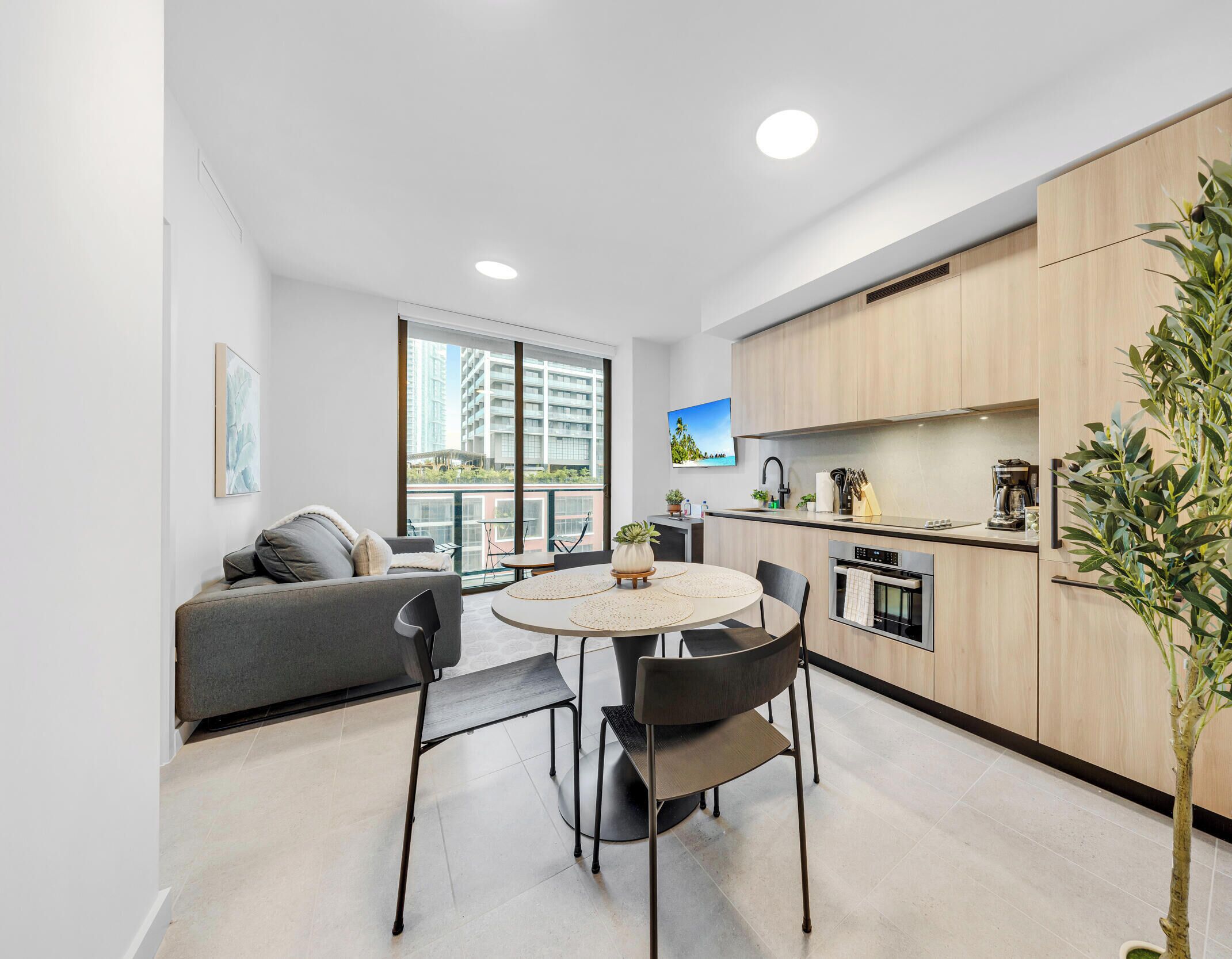 A modern apartment with a dining area, kitchen, and a large window with a city view.