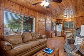 Ein Holzinterieur mit Ledersofa, Korbsessel, Esstisch und Küchenzeile.
