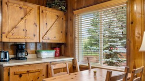 A wooden cabin interior with a dining table, chairs, a coffee maker, and a window with blinds. - Lazy Trout Aspen Cabin (Greer)