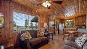 L’intérieur d’une cabane est doté d’un plafond en bois, d’un ventilateur de plafond, d’un canapé, d’une table à manger et d’un coin cuisine.