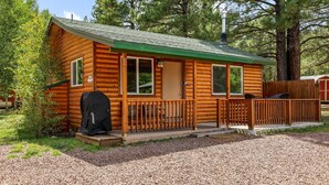 Une cabane en rondins avec un toit végétalisé, une véranda dotée d’une balustrade et un barbecue à l’extérieur.