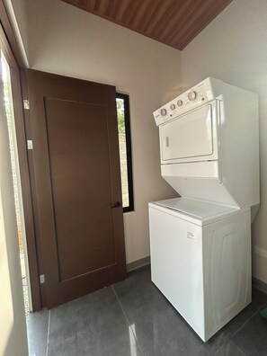 A laundry room with a washing machine and dryer, a brown door, and a tiled floor. - Caroline home 1 (Quepos)