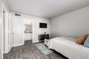 Un dormitorio con cama, mesita de noche, televisor, cómoda y baño con espejo y lavamanos.
