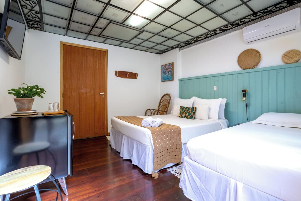 A hotel room with two beds, a wooden door, a ceiling with a grid pattern, and an air conditioning unit.