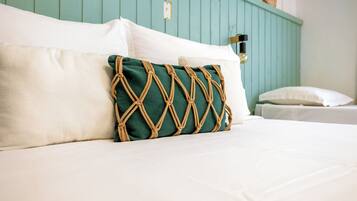A bed with white linens, a green macrame pillow, and a teal headboard.