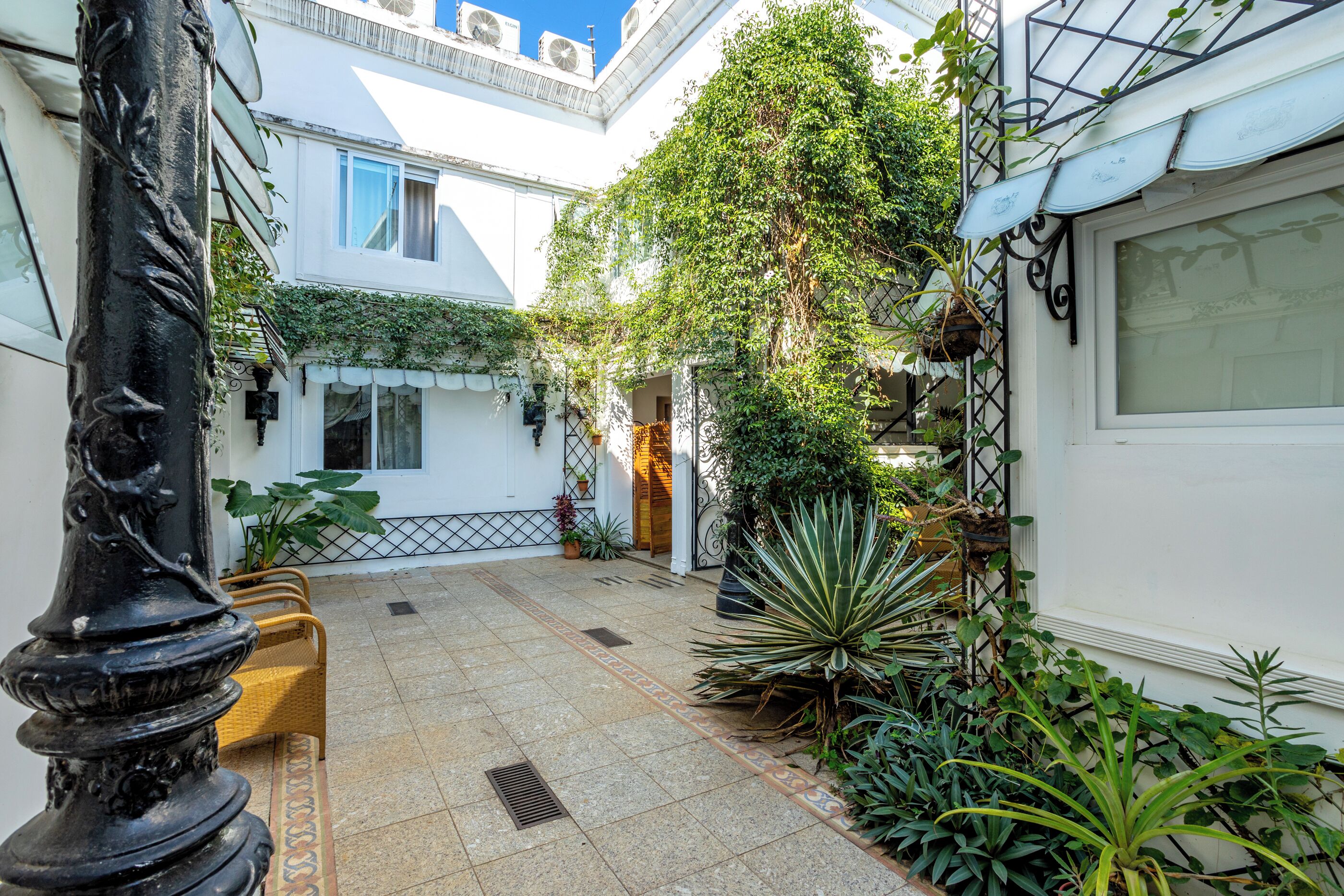 A courtyard with a tiled floor, a bench, potted plants, and a white building with a window.