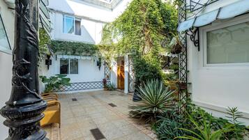 A courtyard with a tiled floor, a bench, potted plants, and a white building with a window.