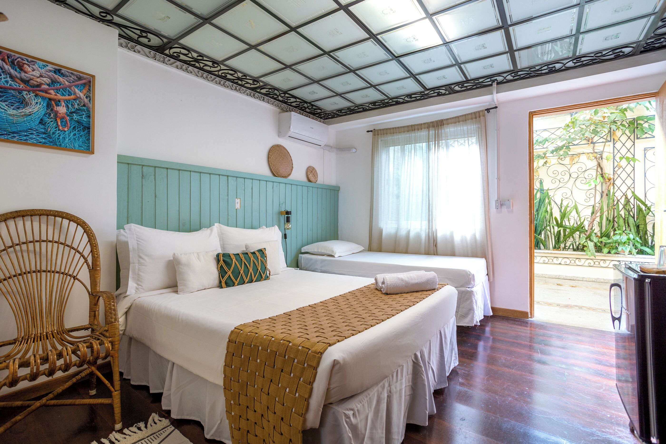 A hotel room with a bed, a chair, a desk, and a view of greenery outside.