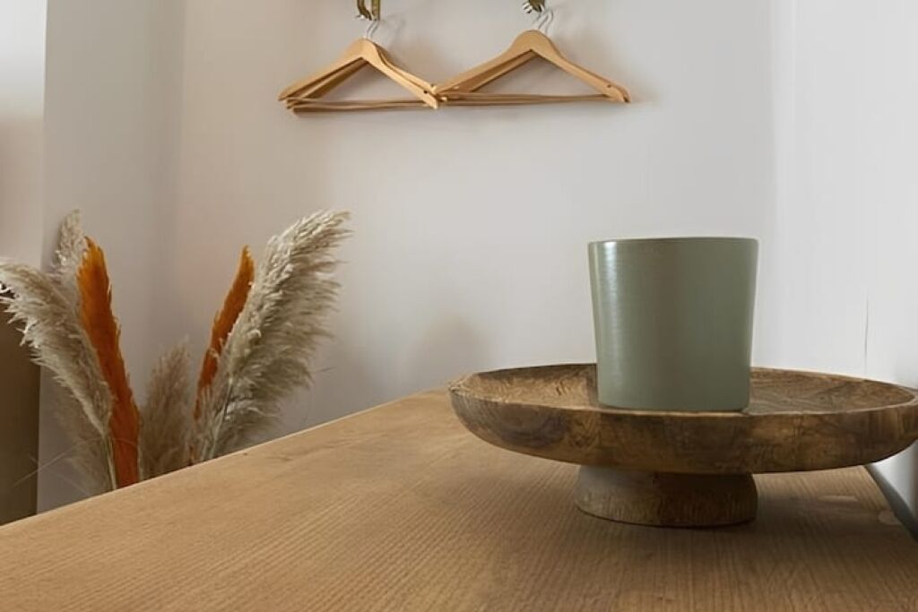 A wooden table with a green cup on a wooden stand, a wooden hanger on the wall, and pampas grass in the background.