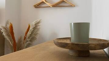 A wooden table with a green cup on a wooden stand, a wooden hanger on the wall, and pampas grass in the background.