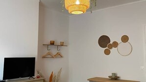 Une pièce dotée d’un téléviseur à écran plat, d’un meuble en bois, d’un luminaire suspendu, d’étagères murales et d’œuvres d’art décoratives accrochées au mur.