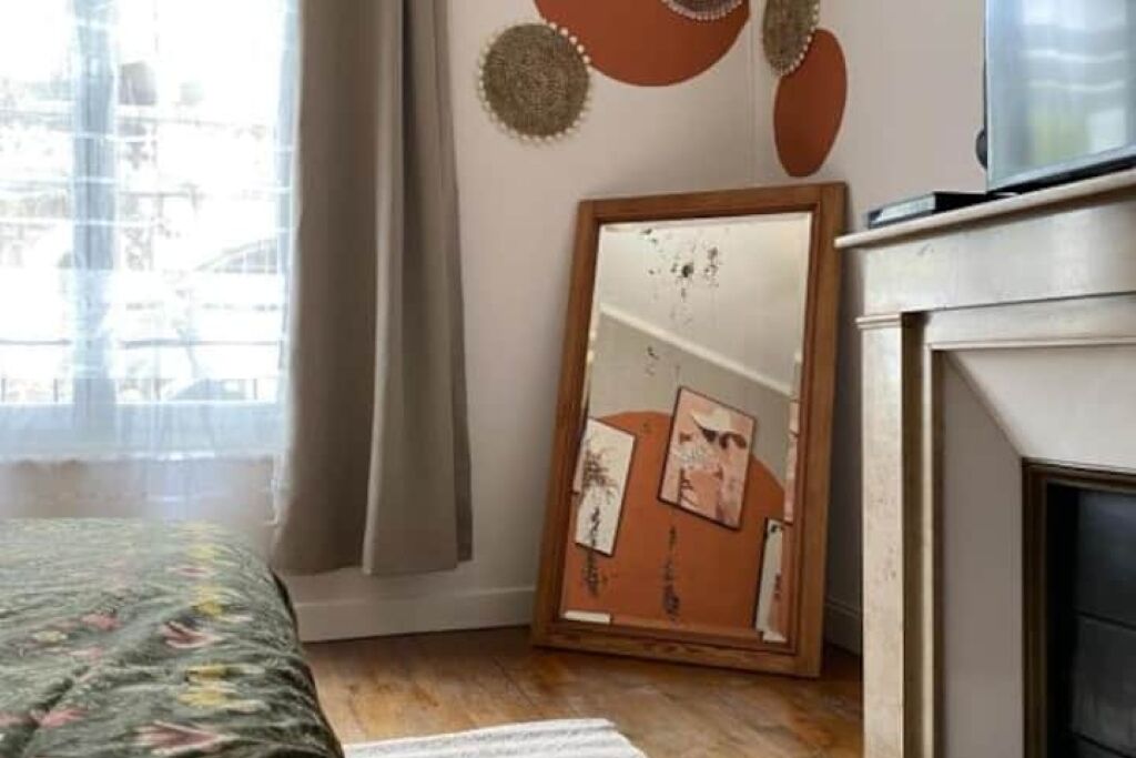 Een slaapkamer met een bed, een spiegel met foto’s, een open haard en een raam met gordijnen.