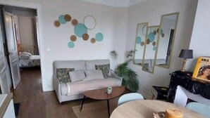 Un salon avec un canapé, une table basse et une table à manger décorée d’une bougie. Un miroir et une plante ornent le mur.