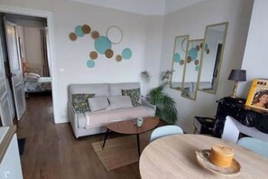 A living room with a sofa, coffee table, and a dining table with a candle. There is a mirror and a plant on the wall.