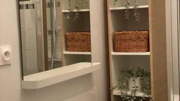 Une salle de bain dotée d'une douche à parois de verre, d'étagères blanches ornées de paniers en osier et d'un miroir qui agrandit l'espace.
