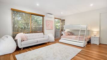 A bedroom with a bunk bed, a sofa, a bedside table, and a window with blinds.