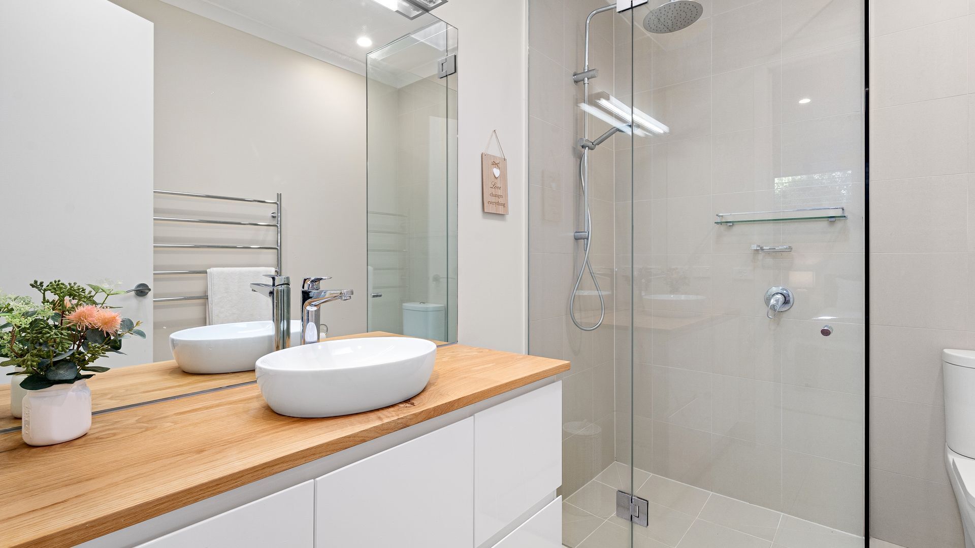 A modern bathroom with a wooden vanity, two sinks, a glass shower enclosure, and a mirror.