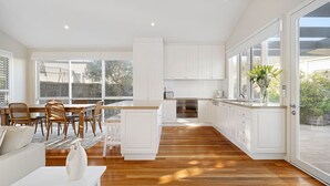 A modern kitchen with white cabinetry, a dining area with a wooden table and chairs, and a large window providing a view of the outdoors.