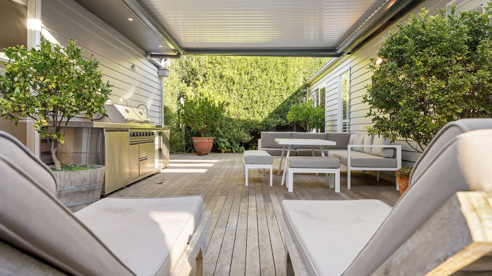 A covered patio with a grill, seating area, and potted plants.