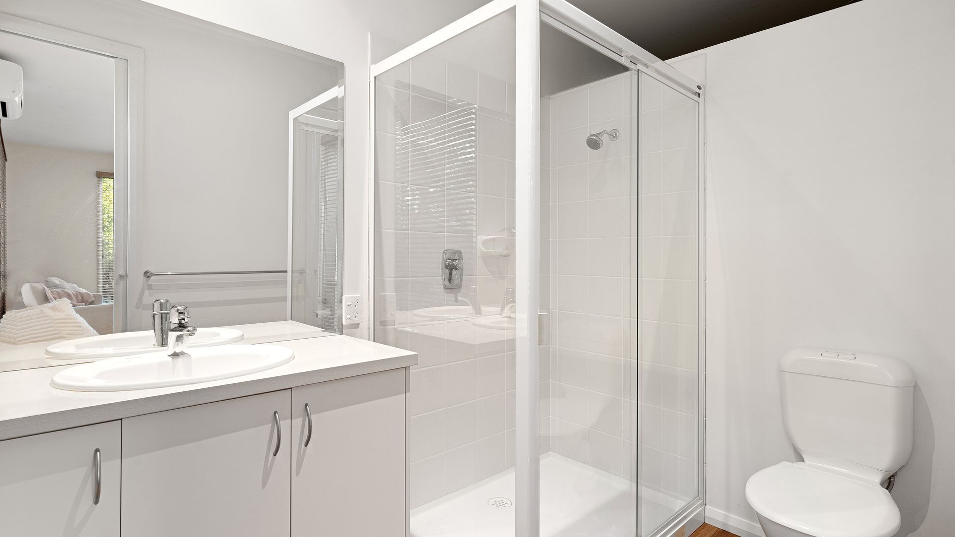 A modern bathroom with a glass shower enclosure, a white toilet, and a vanity with two sinks.