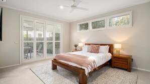A bedroom with a bed, bedside lamps, a ceiling fan, and a view through the window blinds.