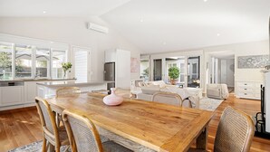 A spacious kitchen with white cabinetry, a wooden dining table, and a large window.