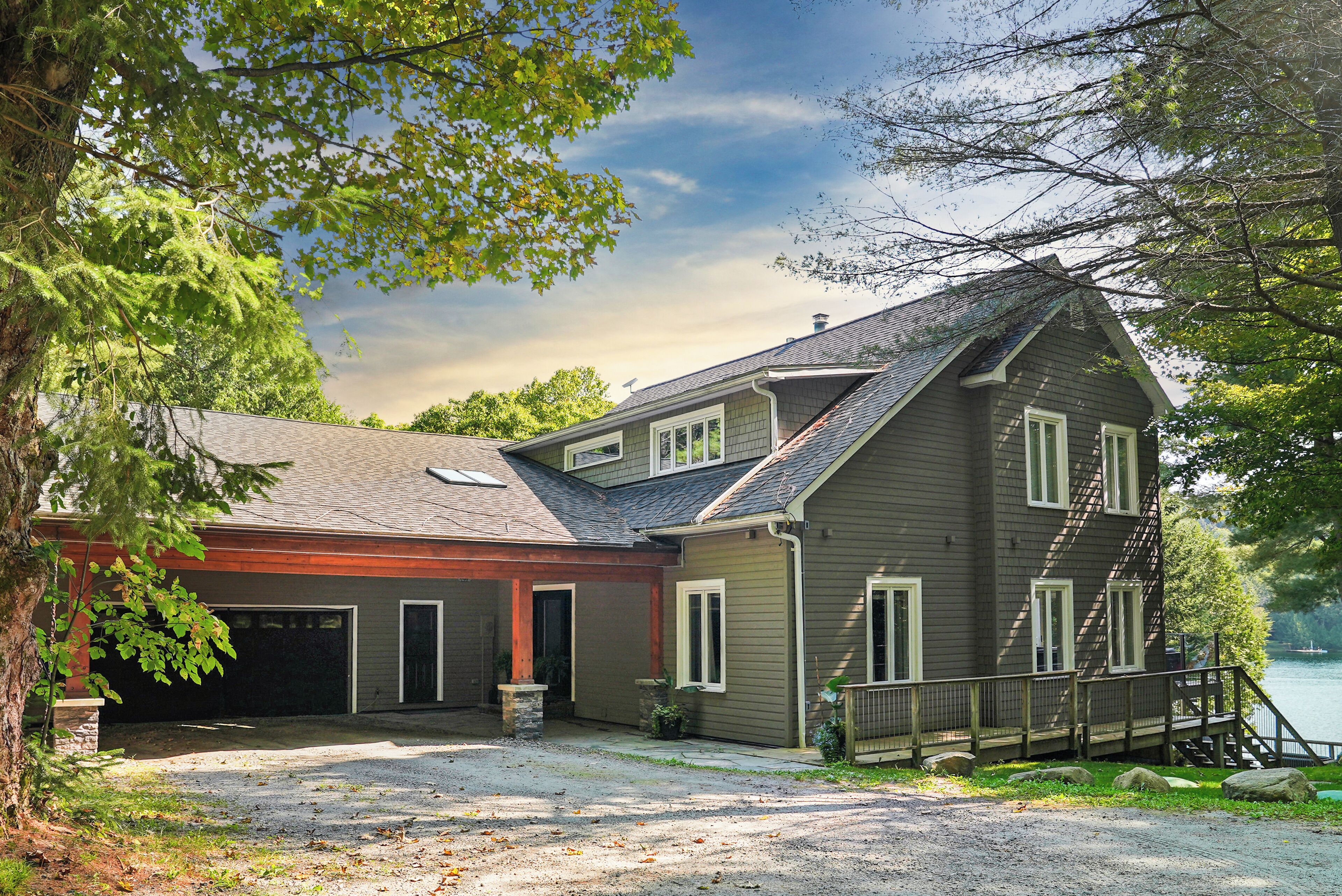 A two-story house with a garage, a covered porch, and a dock extending into a lake.