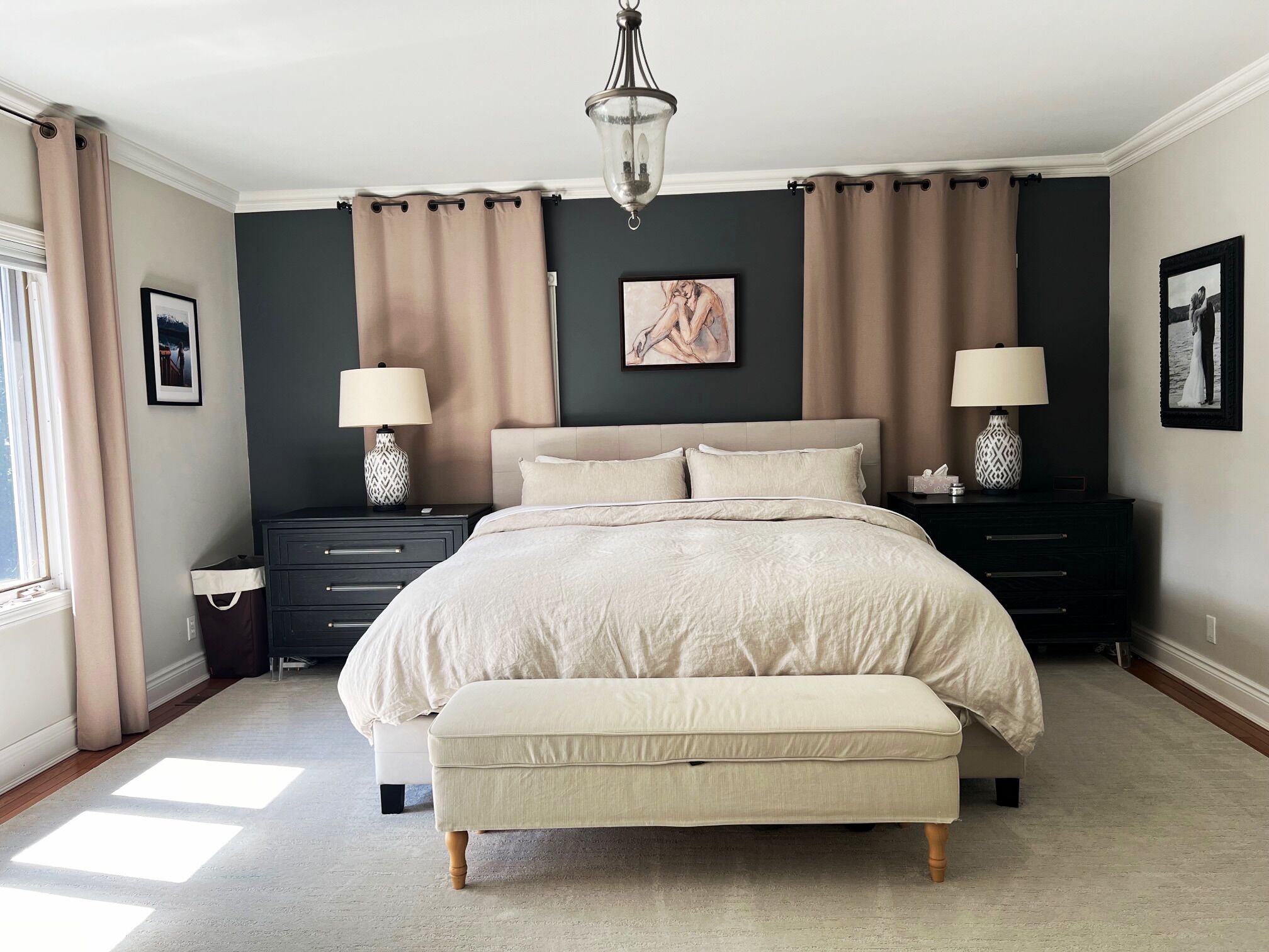 A bedroom with a large bed, two bedside tables with lamps, a nightstand, a window with curtains, and a painting on the wall.