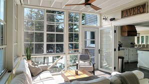 A sunlit room with a large window, a ceiling fan, a sofa, and a kitchen area. - Luxury on Glen Lake (Eagle Lake)