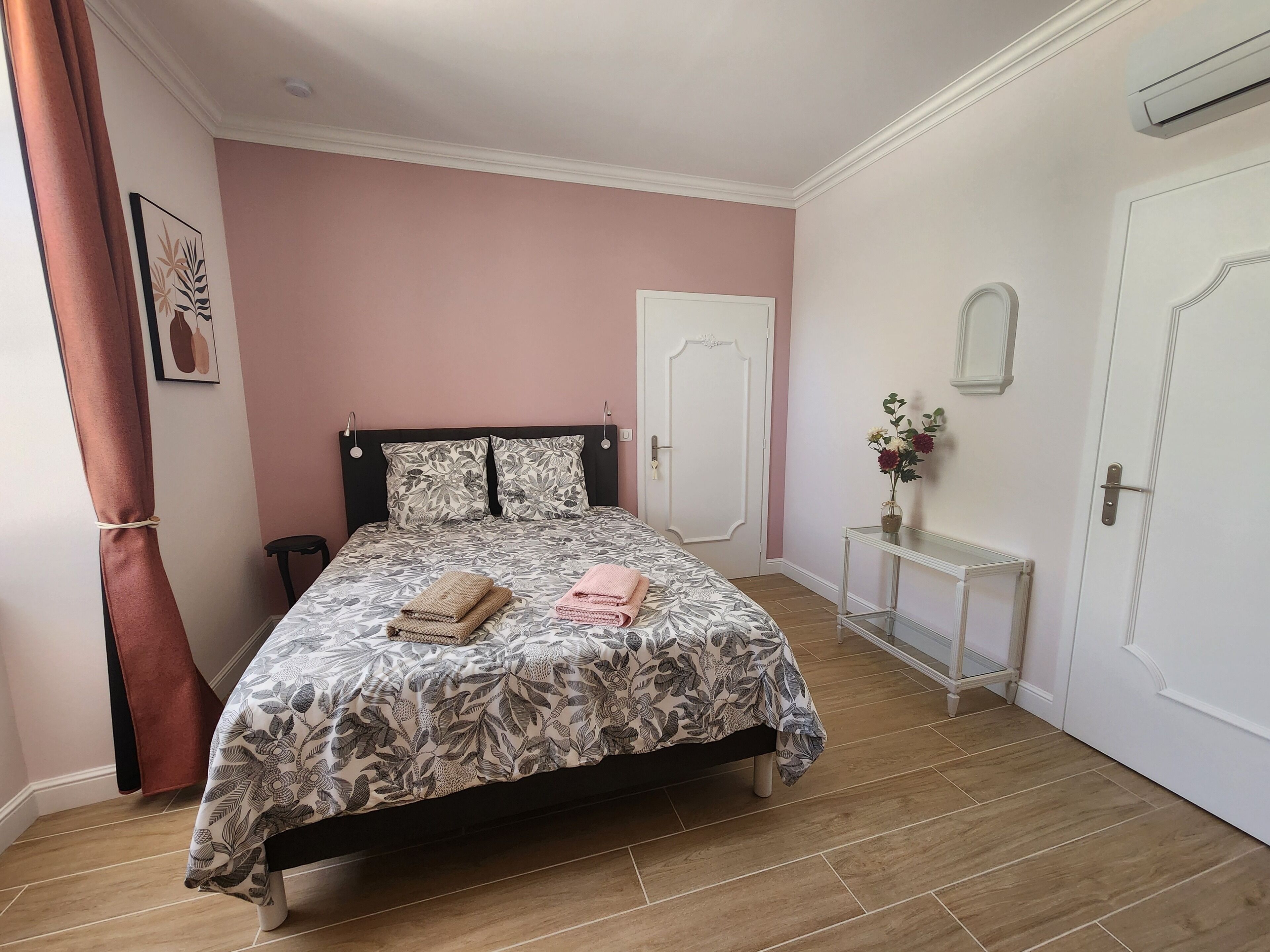 A bedroom with a bed, a bedside table, a door, and a wall-mounted air conditioner.