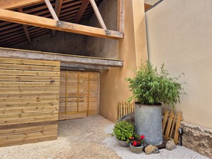 A wooden gate, a large potted plant, a small pot with red flowers, and a metal barrel.