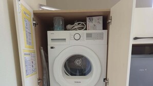 Un lavadero pequeño con dos lavadoras y secadoras apiladas, un refrigerador y una puerta con carteles informativos.