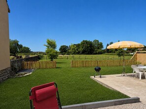 A backyard with a lawn, a barbecue grill, a wooden fence, and a yellow umbrella.