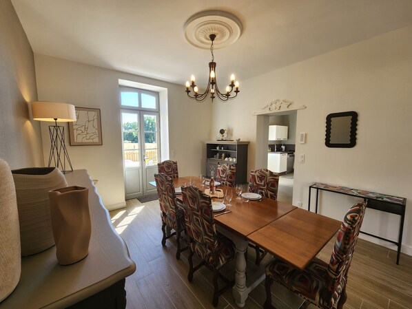 Un coin repas avec une table en bois, des chaises à motifs, un lustre et une vue à travers une porte vitrée.