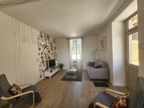 A living room with a flat-screen TV, a sofa, a chair, a patterned wall, and a window with curtains. - Cozy cottage **** "Douceur et rives de Bourgogne" (Palinges)