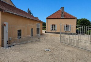 Ein von einer Mauer umschlossener Bereich mit einem Gebäude, das ein rotes Ziegeldach und eine beige Fassade hat.