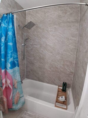 A shower area with a curtain, a handheld showerhead, and a small shelf with toiletries. - Cozy vacation home w/ a spacious outdoor area. Near to great beaches and casinos (Hollywood)