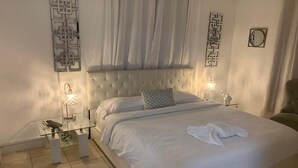 A neatly arranged bedroom with a tufted headboard, a glass bedside table with a lamp, and a bed with a white comforter and a towel. - Cozy vacation home w/ a spacious outdoor area. Near to great beaches and casinos (Hollywood)