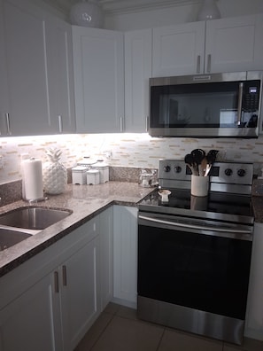 A kitchen with white cabinets, a stainless steel microwave, a stove, and a granite countertop. - Cozy vacation home w/ a spacious outdoor area. Near to great beaches and casinos (Hollywood)