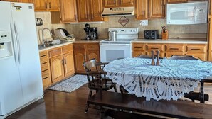 Una cocina con armarios de madera, un refrigerador blanco, un microondas y una mesa con mantel de encaje.